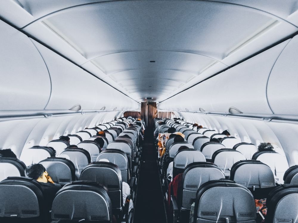 View down the aisle of a passenger aircraft cabin, with rows of seated passengers, where cabin crew carry out the in-flight service