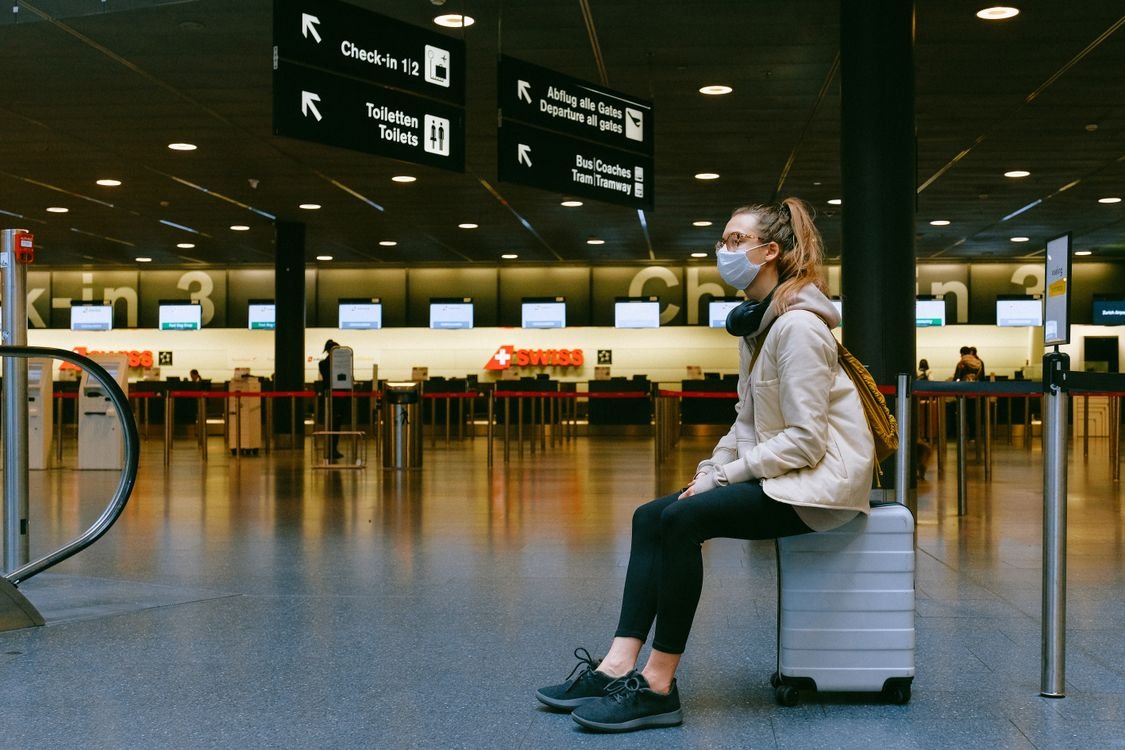 A traveller waiting in an airport departure hall beside the check-in desks, representing the airline environment cabin crew candidates are assessed in on assessment day