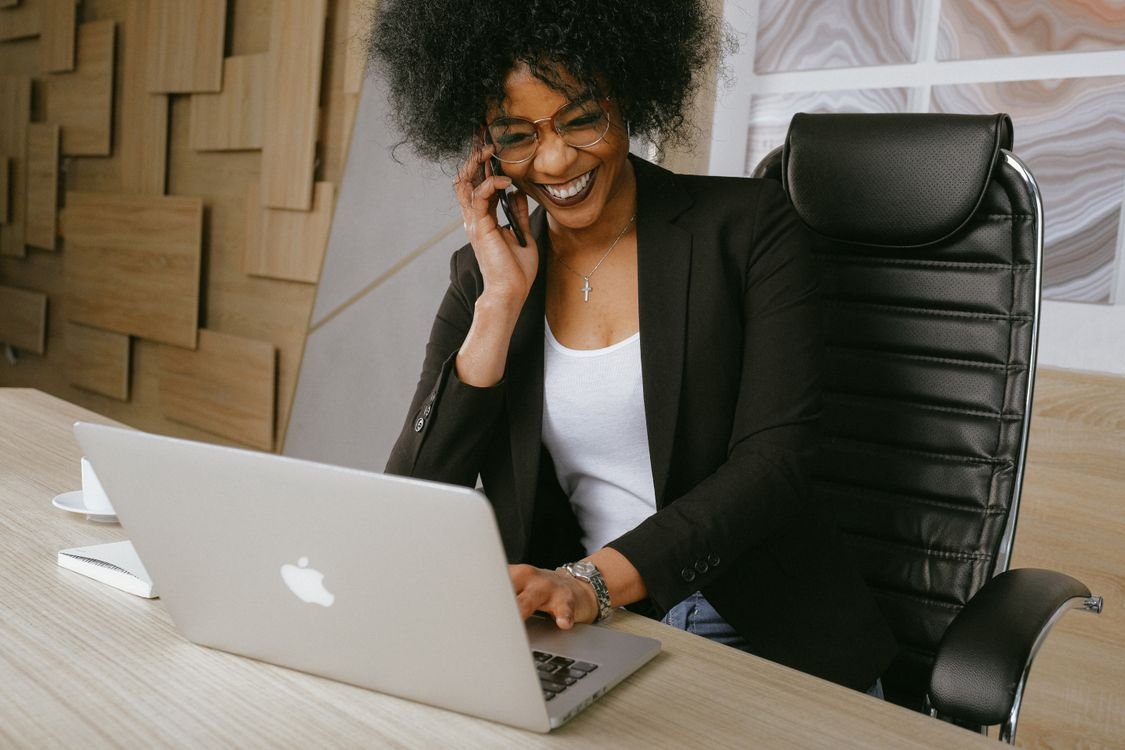 Eine Berufstätige im Blazer arbeitet lächelnd an ihrem Laptop – Online-Business-English im Bildungsurlaub
