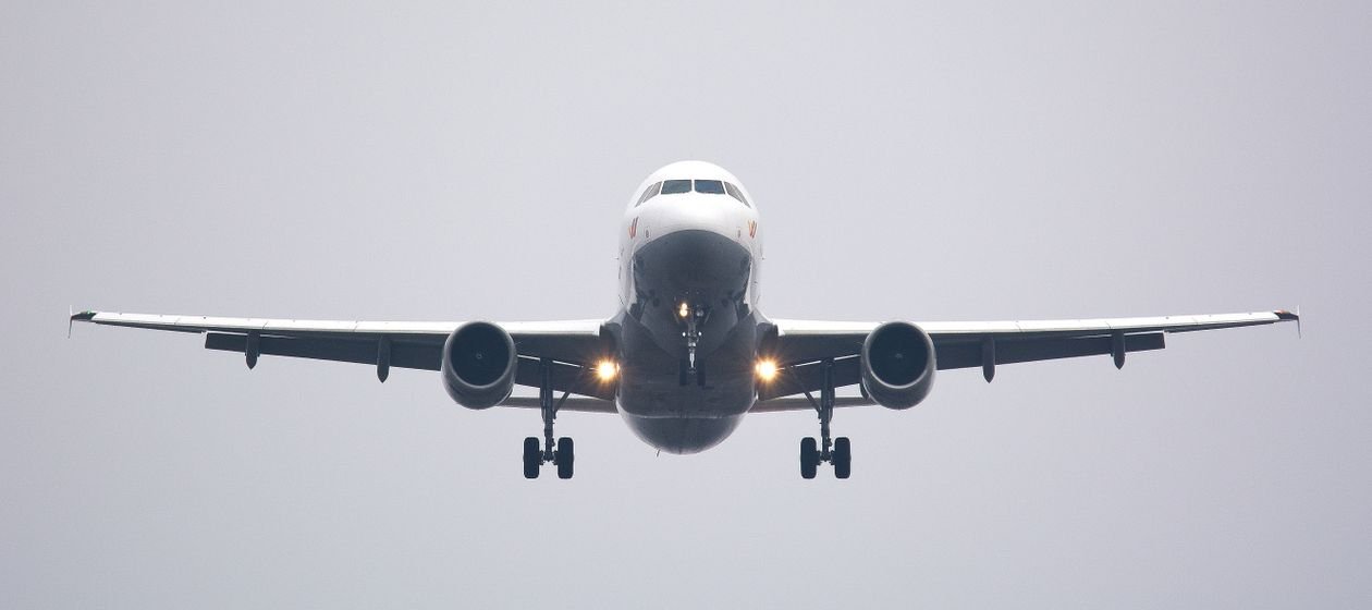 A passenger jet on final approach with its landing gear down and landing lights on, seen head-on against a grey sky