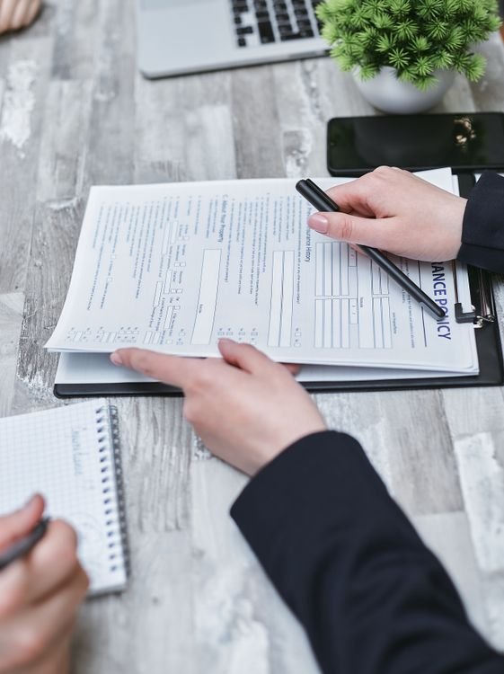 Two insurance professionals reviewing an insurance policy document on a clipboard with a pen at a desk