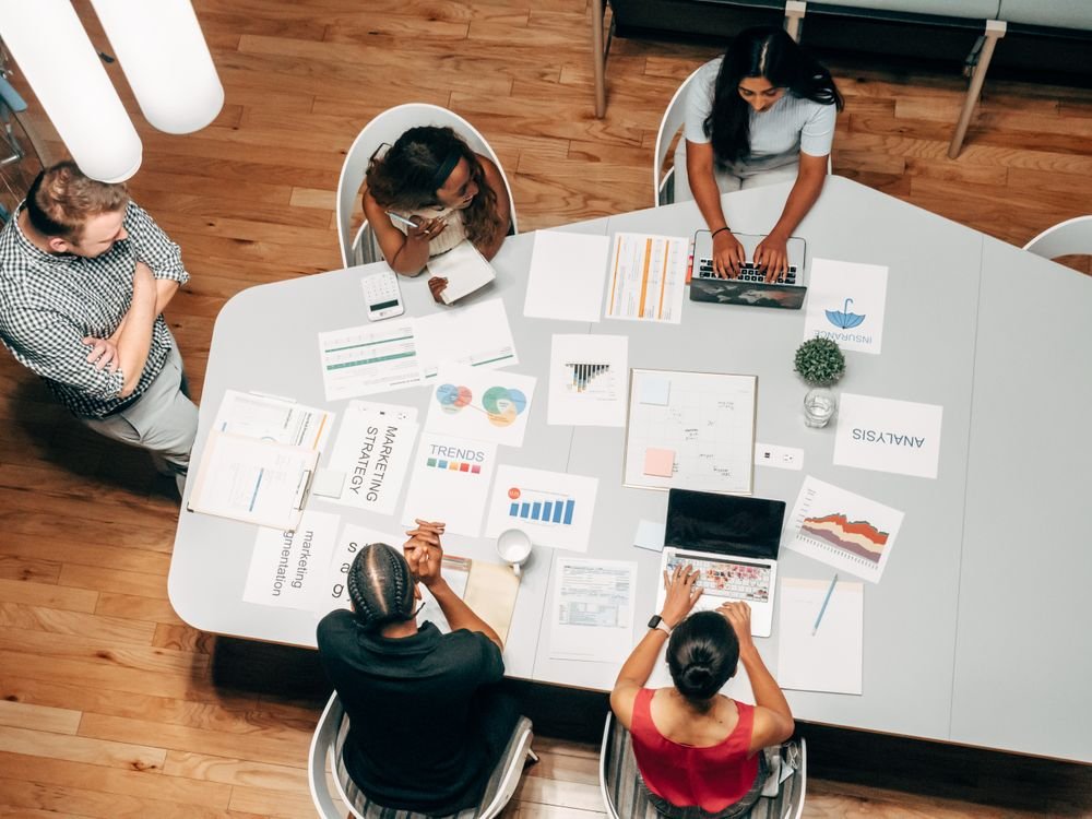 A marketing team meeting viewed from above, with campaign strategy cards, charts and analytics spread across the table