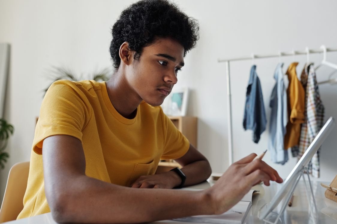 A focused young adult studying English on a tablet at a desk in their bedroom at home