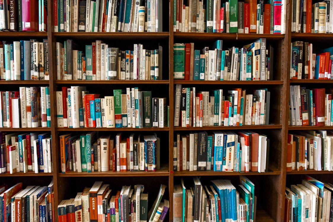 A shelf packed with colourful language-learning books and dictionaries, including grammar guides and coursebooks for beginners