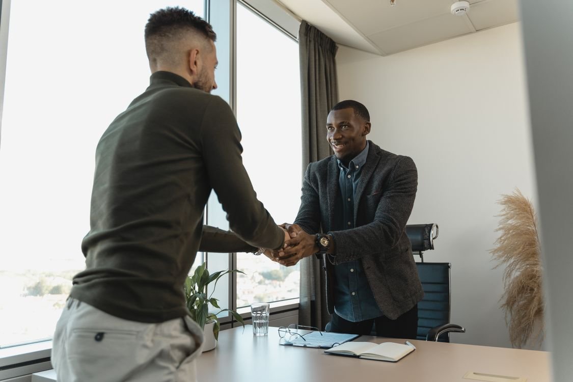 Two professionals meeting one-to-one across an office desk during a performance review, a notebook open between them