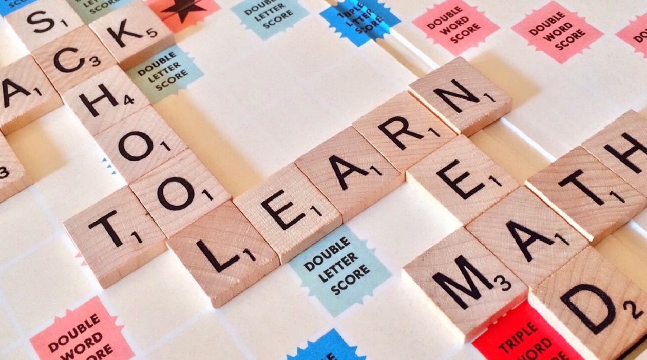 Scrabble letter tiles on a board spelling words including SCHOOL, TO LEARN and READ