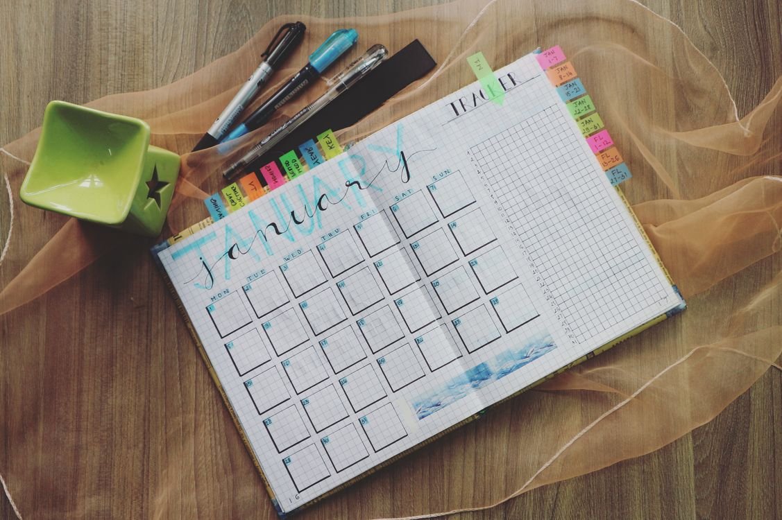 An open monthly planner with a habit tracker, pens and colourful tabs on a desk, used to plan a daily English study routine