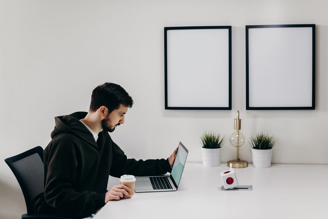 Un professionnel travaille sur son ordinateur portable à un bureau épuré, un café à la main, lors d'un cours d'anglais professionnel en ligne