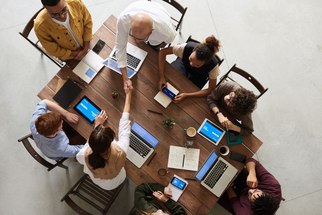 A team of professionals working together around a table with laptops and notebooks in a bright modern office, seen from above
