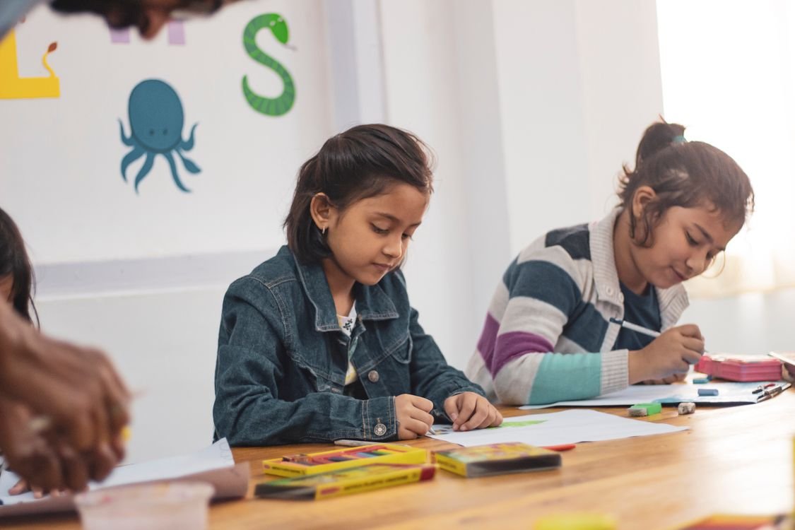 A young child learning English at home, writing at a table with colourful alphabet letters on the wall behind