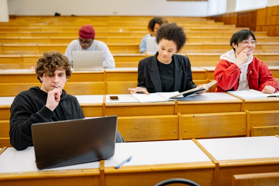 Adult learners studying for IELTS with laptops and open books at desks in a university lecture hall