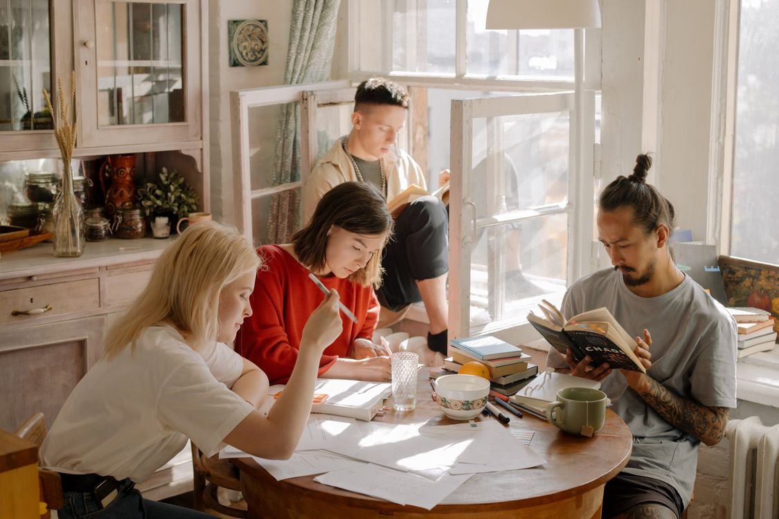 Adult learners studying together at a sunny table with books and notes, working on their IELTS writing