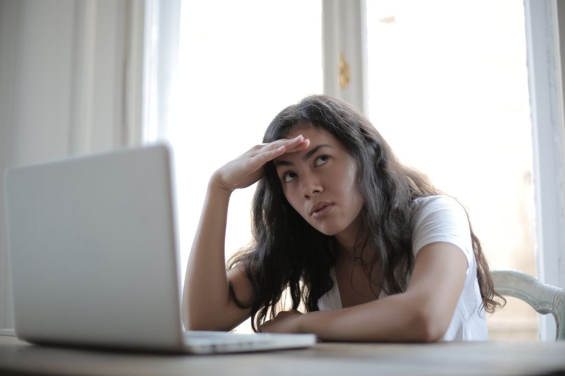 A student sitting at a laptop, pausing to think about how to reword a sentence while writing