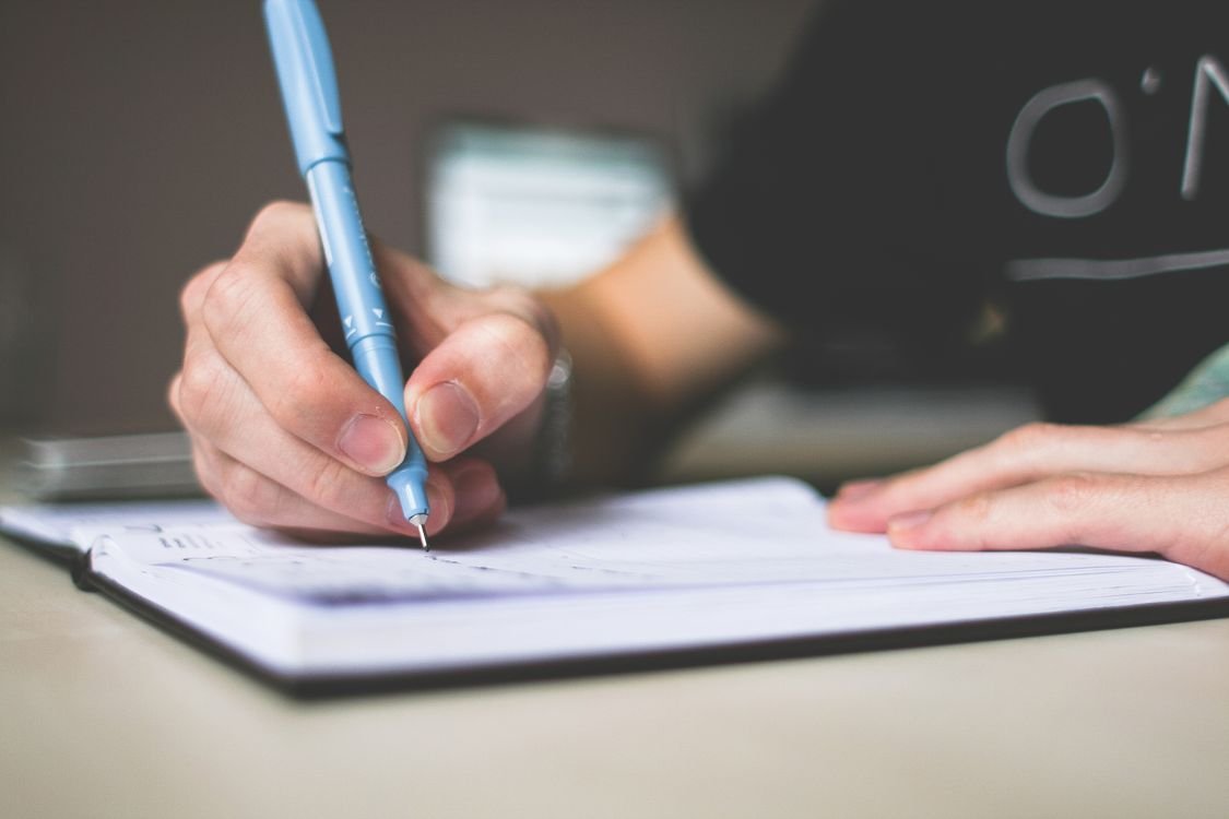A hand writing in a lined notebook while wearing a wristwatch, working against the clock during timed IELTS practice
