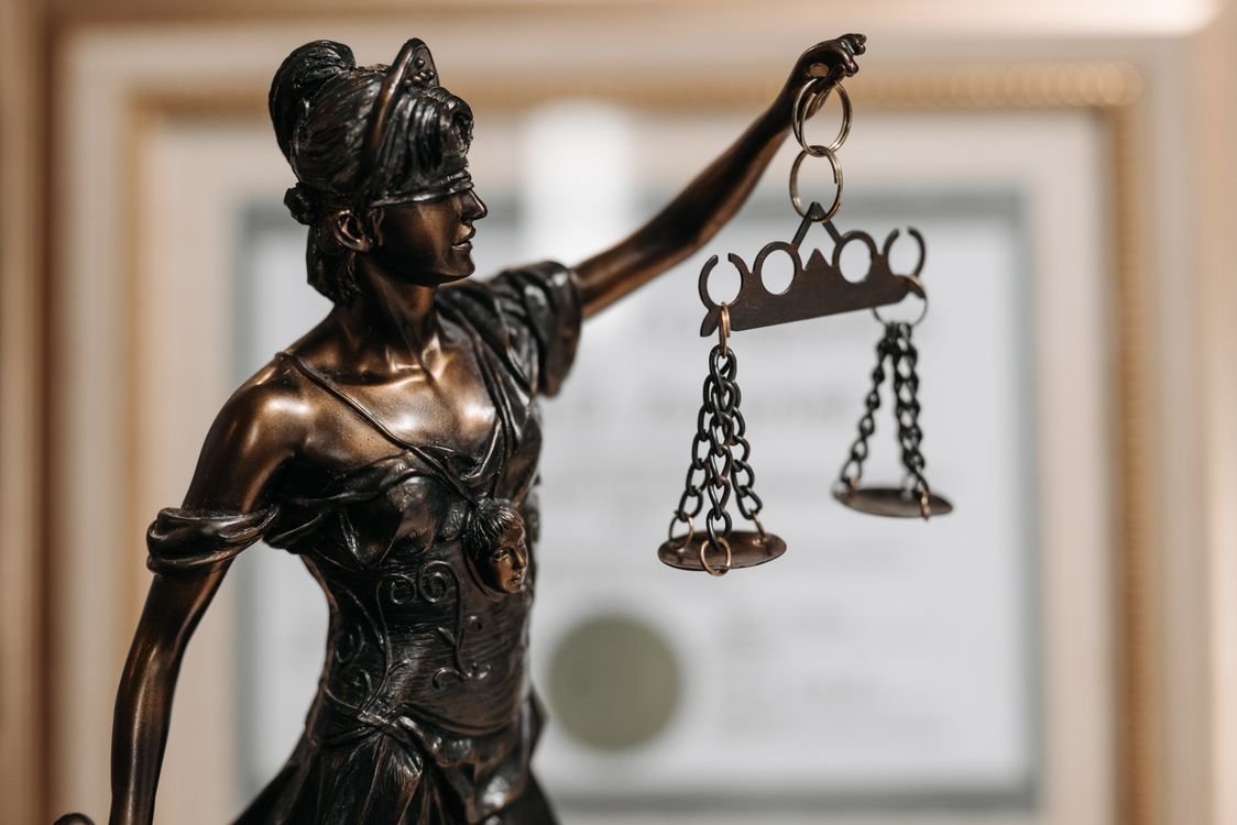 A bronze statue of Lady Justice holding scales, in front of a framed certificate on a wall, representing legal English for lawyers