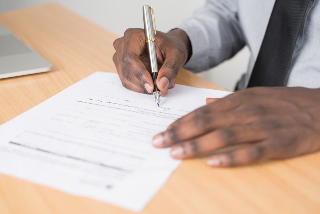 A professional in a shirt and tie signing a formal letter with a pen at a desk