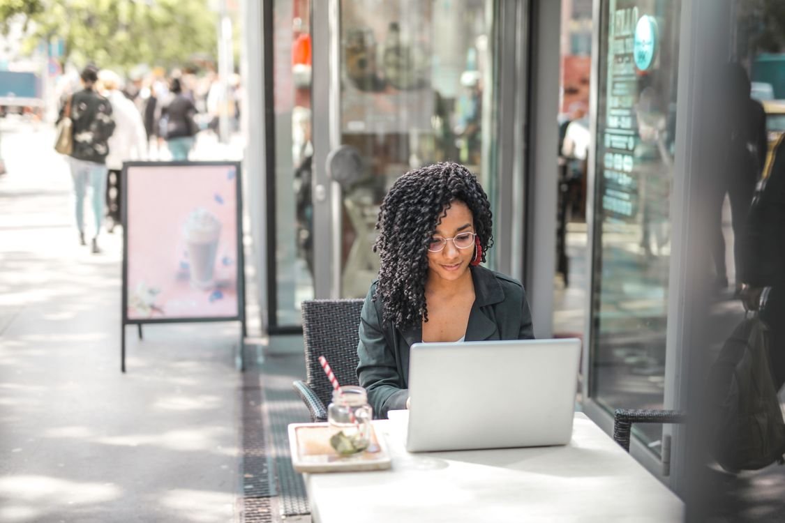 An adult English learner studying on a laptop at an outdoor cafe table, managing everyday situations independently at A2 elementary level