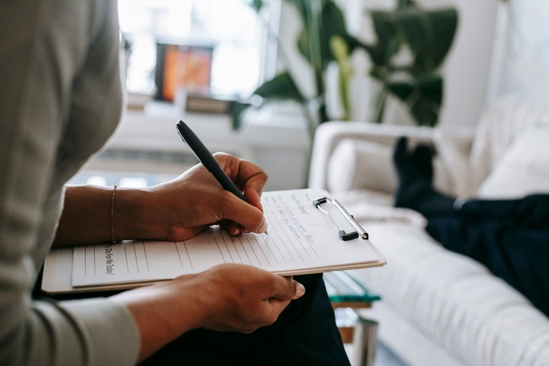 A person writing notes by hand on a clipboard during a meeting